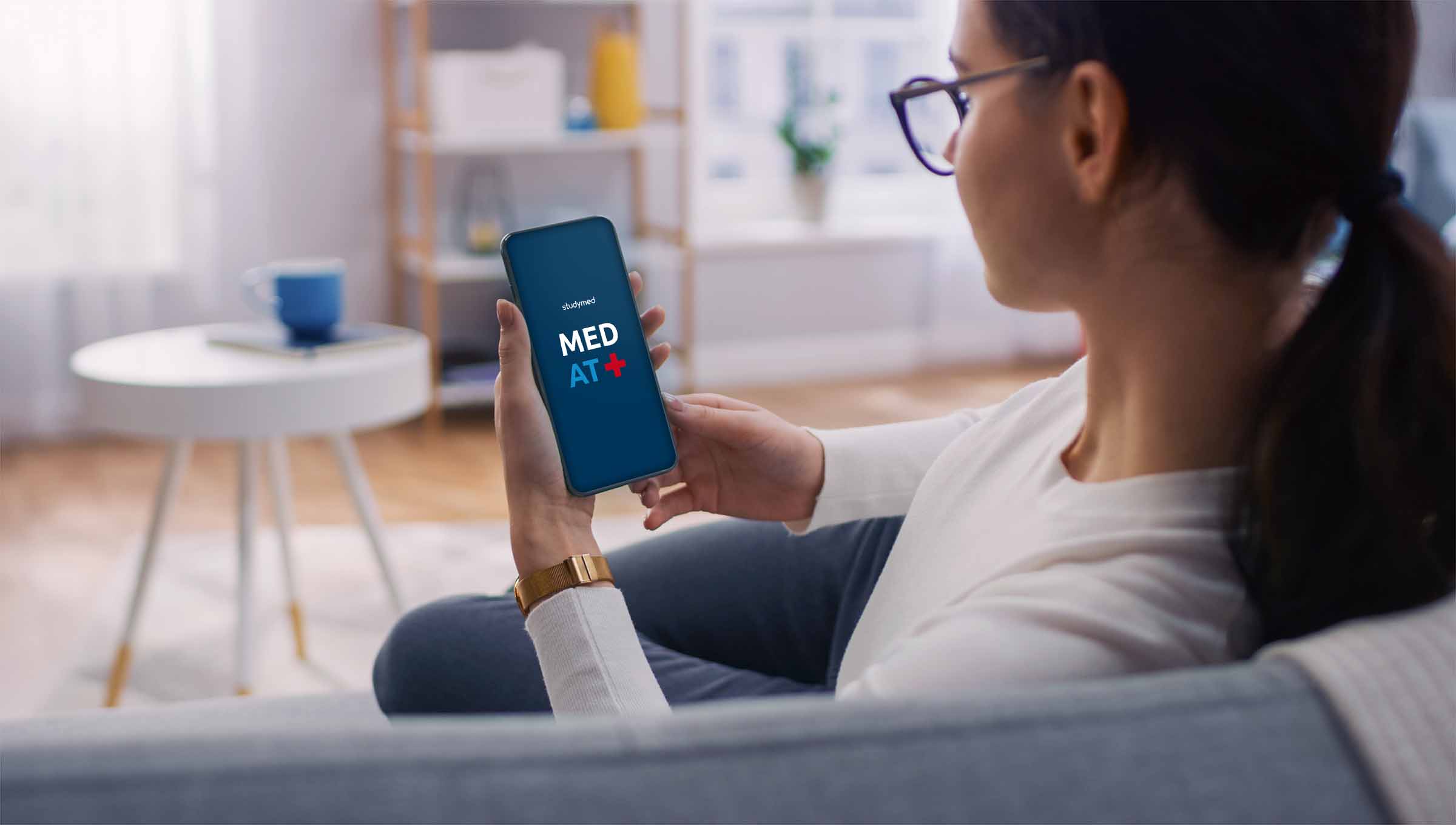 Eine junge Frau auf einem Sofa spielt mit der MedAT+ App von studymed